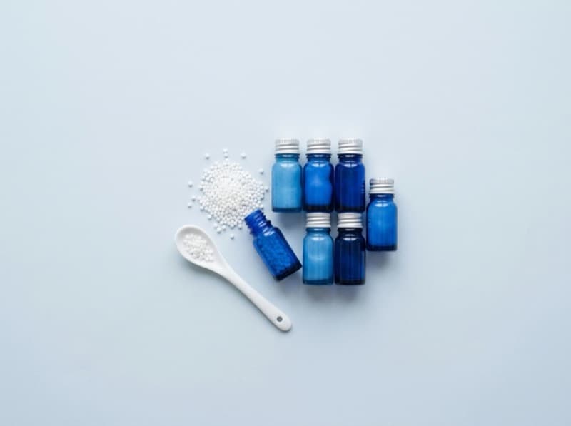 Globuli, blaue Arzneifläschchen und Porzellanlöffel